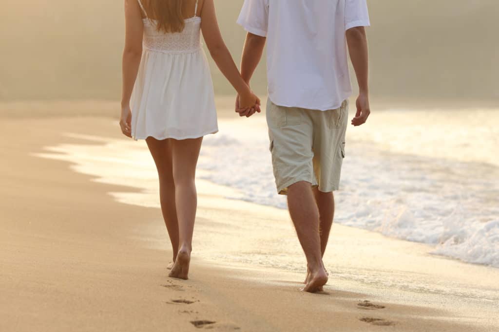 Back view of a couple taking a walk holding hands on the beach at sunrise